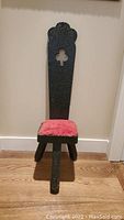 Front view of tri-leg chair showing carved tall backrest with clover-shaped cutout and pink velvet cushion seat.