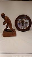 Photo showing wooden hockey player carving and round framed plate side by side on white background.