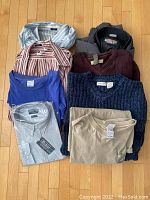 Photo showing various men's clothing items laid out including jacket, knitted sweaters, t-shirts, and button-up shirts.