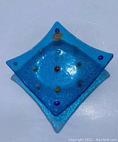 Top-down view of the square light blue Murano glass dish showing the colorful embedded millefiori dots and Murano Italy product label.