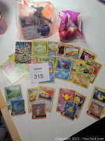 Photo showing assorted Pokémon cards spread out, including holographic and standard cards, along with two sealed McDonald's Pokémon toys in original packaging.