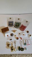 Full display of all items including the wooden box, fabric patches, pins, badges, and keychains laid out on a white background.