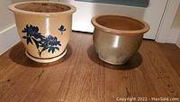 Two pottery plant pots placed on wooden floor, one with floral design and tray, one plain