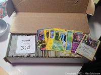 Open white storage box filled with a large quantity of Pokemon trading cards, all standing upright. Several cards are pulled out in front displaying different Pokemon characters and some energy cards.