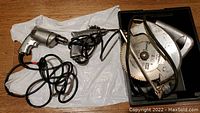 All three tools shown laid on floor: one circular saw and two electric drills with cords.