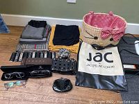 Photo showing assorted scarves folded in colors, multiple belts, two pairs of eyeglasses, small black coin purse, a Jacqueline Conoir tote bag, and a woven basket-style bag.