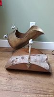 Photo of copper and brass firewood caddie with wooden and brass handles alongside the scuttle bucket on wood floor.