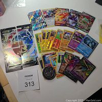 Photo showing an assortment of holographic Shiny Pokemon cards including a 4-piece VMAX set, single V and VMAX cards, and holographic cards in multiple languages.