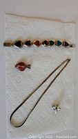 Photo of the bracelet with seven heart-shaped stones, the heart pendant, and the silver necklace on a white paper towel.