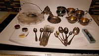 Wide view of all silverplate basket, flatware, utensil holder, shell dish, sugar bowls, creamers and spoons on white cloth