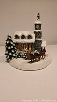 Front angle showing church, clock tower, lighted windows, horse, sleigh, pine trees with snow.