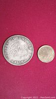 Photo showing front side of the United States Liberty Token alongside a Canadian loonie coin for size comparison.