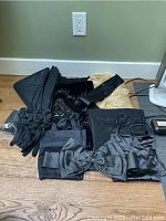 Photo showing various black vintage clothing items and accessories on floor including slips, scarves, gloves, and belts.