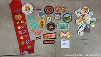 Full arrangement of red sash with sewn patches spread alongside assorted round and square button pins on floor