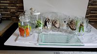 Full lot display showing all glasses, jars, bowls, plates, and serving plate arranged on white cloth with kitchen backsplash background.