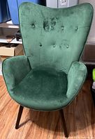 Front view of the green velvet armchair showing button tufted backrest and armrests.