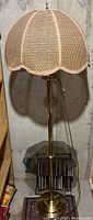 Full view of the floor lamp showing its brass base, pole, and the woven rattan lampshade.