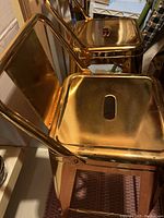 Top angle view of two gold metal bar stools showing seats and backrests, reflective gold surface.