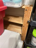 Side view showing wooden vertical support with bolts and three wooden shelves filled with some storage bins around it.