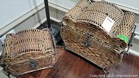 Two baskets on a wooden floor, showing a medium and small basket with woven wicker and metal latch locks.