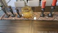 Photo showing five metal candle holders and an amber glass vase on a dining table.