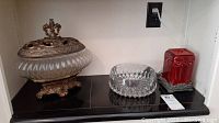Ornate lidded canister, clear glass bowl, and red ceramic container on a shelf