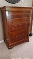 Front angled view of tall wood chest of drawers with five drawers and round knobs