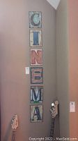 Six distressed metal wall plaques spelling 'CINEMA' vertically mounted on wall