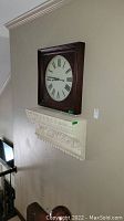 Photo of the wall clock hung above the mantel shelf, showing the dark wooden frame and clock face with Roman numerals.