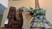 Front view of three brown decorative vintage-style suitcases stacked next to black metal Eiffel Tower décor with faux greenery