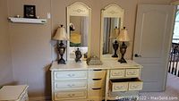 Full view of cream white dresser with two mirrors and part of matching nightstand, showing drawer and mirror details.