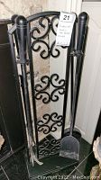 Fireplace tools hanging on decorative black metal stand with scrollwork in background.