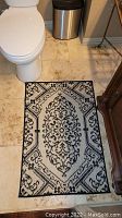 Black and white patterned floor mat placed on a tile floor in a bathroom setting