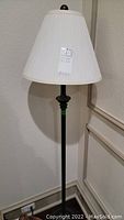 Full view of the black metal floor lamp with white pleated lampshade, showing overall design and condition.