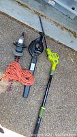 Overview of the two hedge trimmers, blower, and orange extension cord laid on concrete