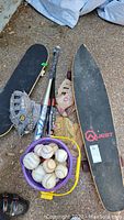 Lot contents include 2 skateboards, 3 baseball bats, 4 gloves, and a bucket of baseballs shown from above on ground.