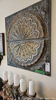 Large decorative square wall plaque with circular floral relief motif and leaf corner accents, mounted on wall near candles