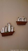 Image of two brown carved wooden wall shelves displaying multiple angel figurines including wire-winged and Precious Moments styles against a beige wall.