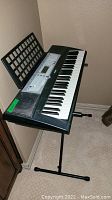 Full view of Yamaha keyboard on adjustable black metal stand with music stand behind.