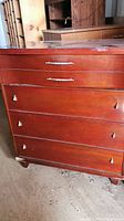Front view of reddish-brown wooden dresser with four drawers showing metal handles and surface wear.