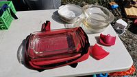 Overview of all cooking bowls, baking dish, silicone holders, and carrying bag on white table outdoors