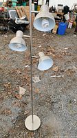 Floor standing light showing three lamp heads with compact spiral CFL bulbs and metal lampshades.