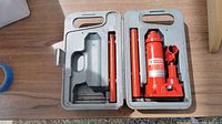 Top view of the gray plastic case with hydraulic bottle jack and two extension rods inside.
