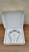 Electric neck massager device in white plastic with charging dock inside an open white box.