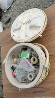 Open round sewing basket showing various sewing supplies inside compartments