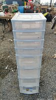 Full view of white plastic 8 drawer storage tower outdoor on gravel surface.