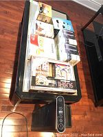 Overview photo of lot items including IonicPro air cleaner, sushi set, popcorn maker, cappuccino press, fondue set, mugs, Slap Chop chopper on glass table with wood floor background