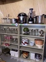 Wide shot of metal shelves holding glass jars, kitchen appliances including pressure cookers, food processor, slow cooker, toaster, and cooking pots.
