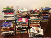 Photo of large assortment of stacked books of various genres on floor next to wall, showing multitude of titles and colors and sizes