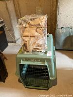 Photo of large turquoise Vari dog kennel with metal door and ventilation grilles, with small white wire cage on top filled with fabric padding.